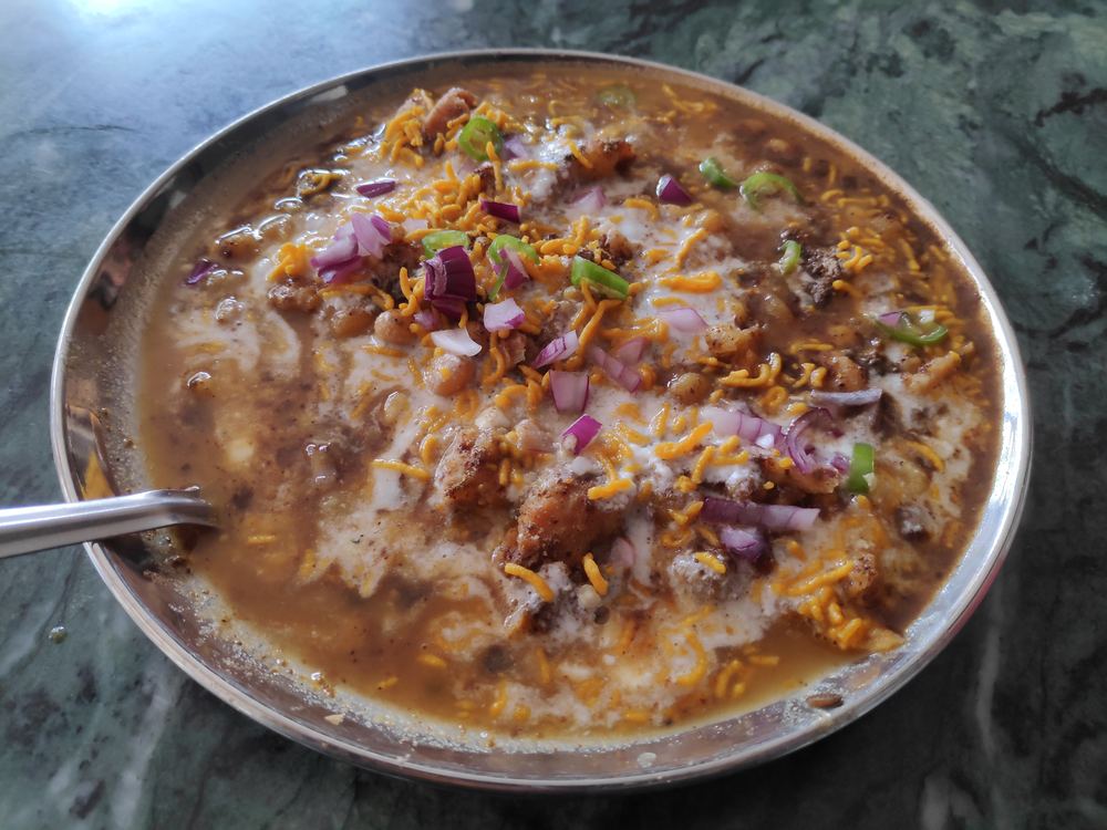 Samosa chaat topped with chickpeas, yoghurt and tamarind chutney